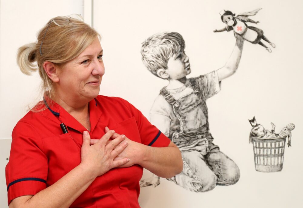 infermiera posa davanti l'opera "Game Charger" di Banksy