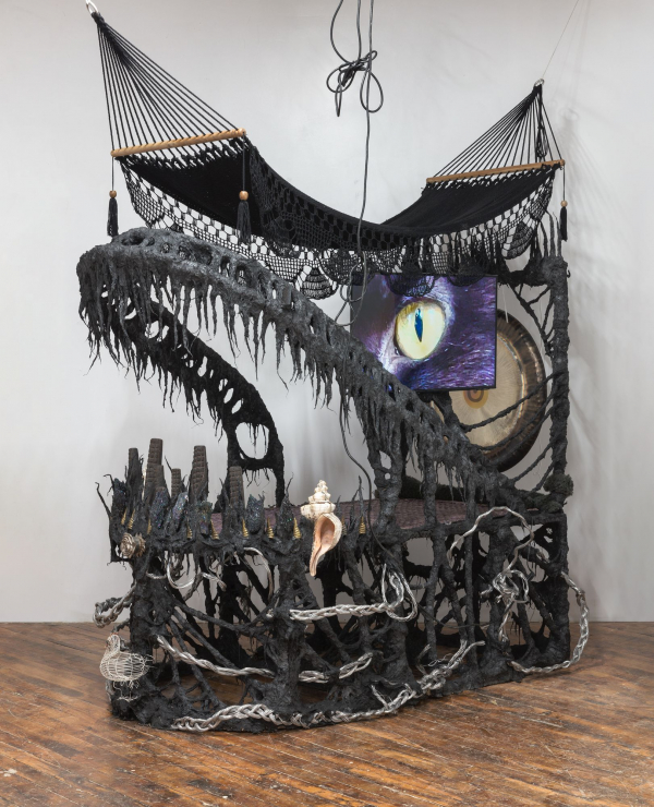 Guadalupe Maravilla, Disease Thrower #0, 2022. Gong, hammock, LCD TV, ceremonial ash, pyrite crystals, volcanic rock, steel, wood, cotton, glue mixture, plastic, loofah, objects collected from a ritual of retracing the artist's original migration route. Courtesy of the artist and P·P·O·W, New York. © Guadalupe Maravilla. (Photo: Stan Narten)