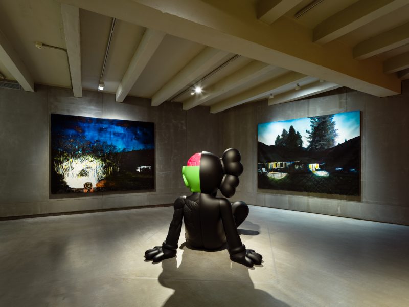 La scultura di Kaws osserva Going Home for Christmas (2023) e Home and Away II (2021) di William Mackinnon