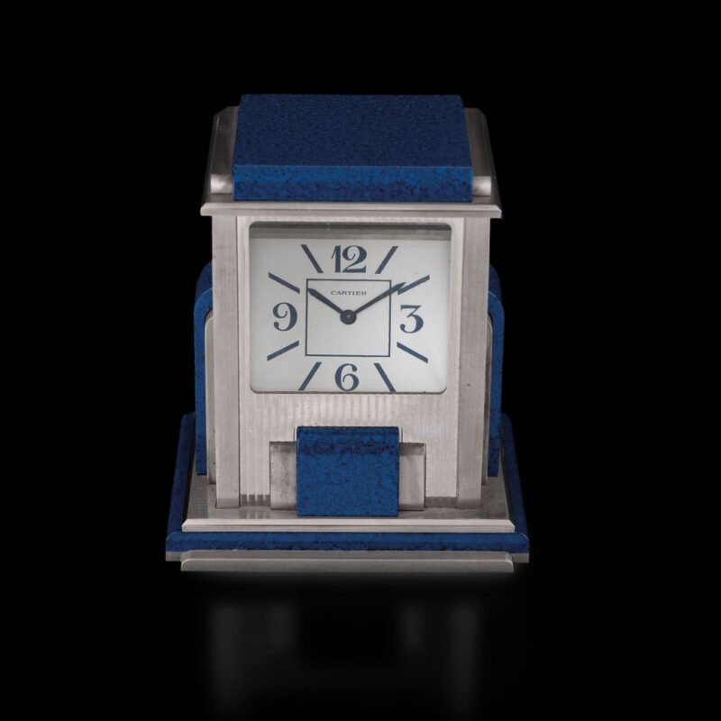 Lotto 221, CARTIER PRISM MYSTERY, OROLOGIO DA APPOGGIO O DA SCRIVANIA IN LAPISLAZZULI, SVIZZERA 1980 CIRCAcassa a forma di parallelepipedo in metallo argentato arricchito da eleganti placche in lapis, quadrante frontale in cristallo, con quadrante interno firma- to Cartier, movimento al quarzo da testare. Alt. 10,5 cm, larg. 9 cm, prof. 7.5 cm. Questo orologio misterioso di Cartier, noto come orologio "a prisma", è un'opera di ingegneria eccezionale e di arte raffinata. Realizzato in un elegante sti- le Art Déco con placche in lapislazzuli, questo orologio a prisma è dotato di prismi e specchi in cristallo di quarzo che permettono al quadrante, che è na- scosto nella base, di diventare visibile attraverso la finestra trasparente, ma solo da una certa angolazione. Questo ingegnoso design fu sviluppato e bre- vettato per la prima volta nel 1937 da Gaston Cusin, che si ispirò a un periscopio. Cartier ha prodotto diversi modelli di orologio a prisma, molti dei quali realizzati con materiali di pregio e design eleganti come questo. Stima € 1.000 - 1.500 Aggiudicato € 4.000 - Wannenes